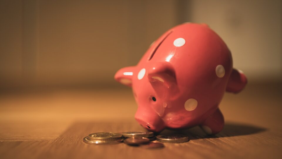 A pink piggy bank on a table surrounded by coins.